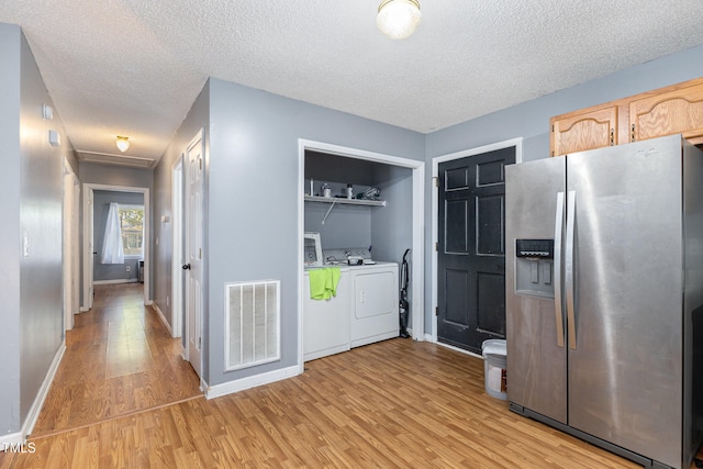 kitchen with stainless steel refrigerator with ice dispenser, independent washer and dryer, a textured ceiling, light brown cabinetry, and light hardwood / wood-style floors