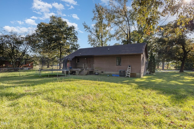 back of property with a trampoline and a yard