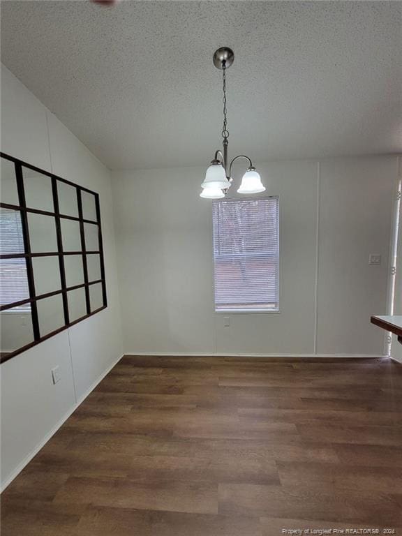 unfurnished dining area featuring a notable chandelier, dark hardwood / wood-style flooring, and a textured ceiling