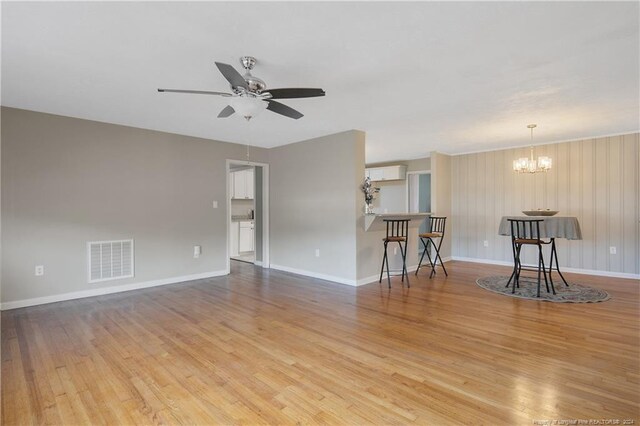 unfurnished living room featuring ceiling fan with notable chandelier, wood walls, and light hardwood / wood-style flooring