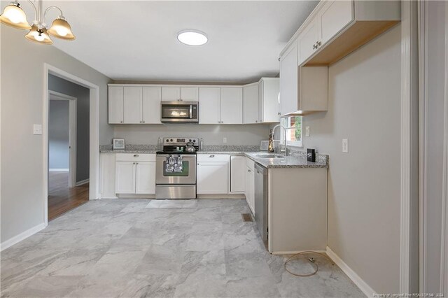 kitchen featuring white cabinetry, sink, light stone counters, pendant lighting, and appliances with stainless steel finishes