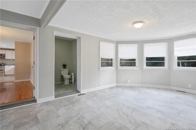 unfurnished bedroom featuring a textured ceiling, ensuite bathroom, ornamental molding, and light hardwood / wood-style floors