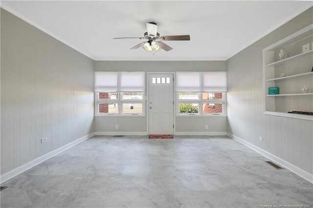 spare room with built in shelves, ceiling fan, crown molding, and wood walls