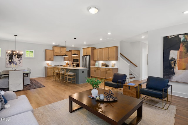 living room with an inviting chandelier, sink, and light hardwood / wood-style flooring