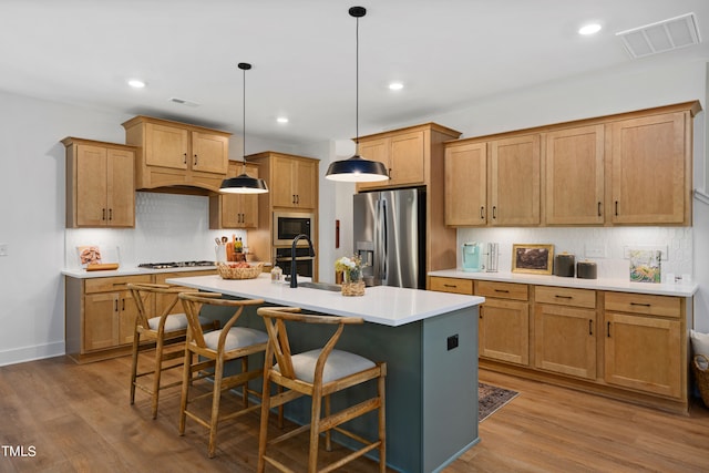 kitchen with a breakfast bar, sink, decorative light fixtures, appliances with stainless steel finishes, and an island with sink