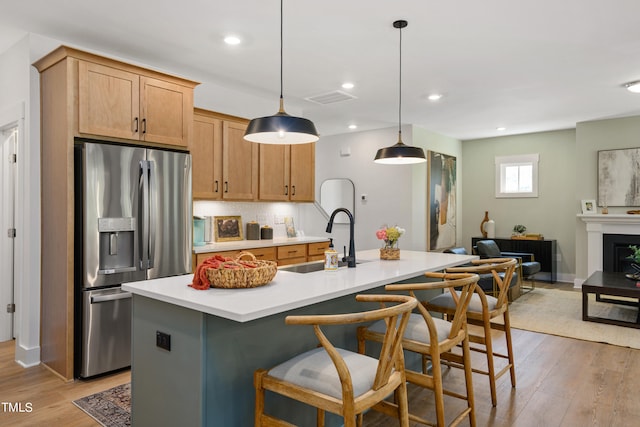 kitchen featuring a kitchen island with sink, sink, stainless steel fridge, and decorative light fixtures