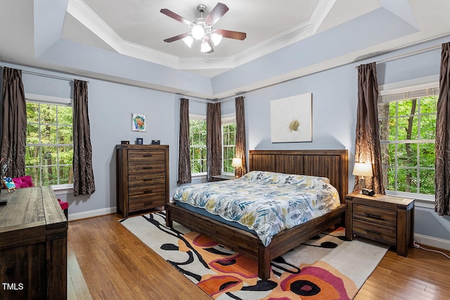 bedroom with light hardwood / wood-style floors, multiple windows, a tray ceiling, and ceiling fan