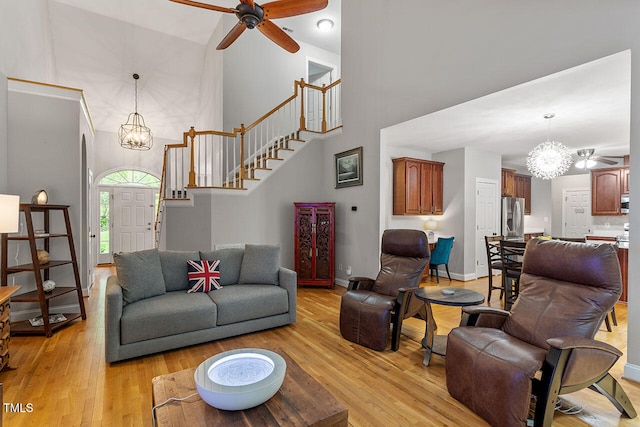 living room featuring light hardwood / wood-style flooring, a towering ceiling, and ceiling fan with notable chandelier