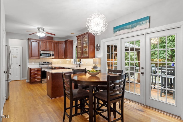 dining space featuring light wood-style flooring, ceiling fan with notable chandelier, and french doors