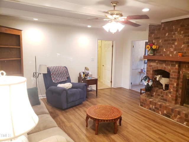 living room featuring ceiling fan, wood-type flooring, ornamental molding, and a brick fireplace