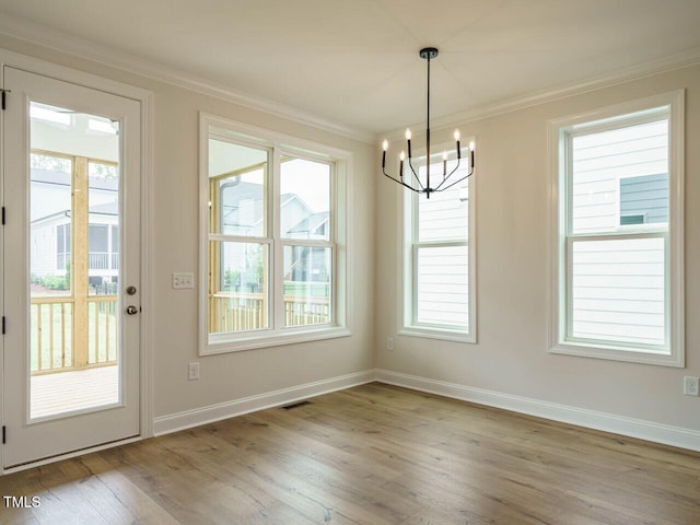 unfurnished dining area featuring a chandelier, hardwood / wood-style floors, a healthy amount of sunlight, and ornamental molding