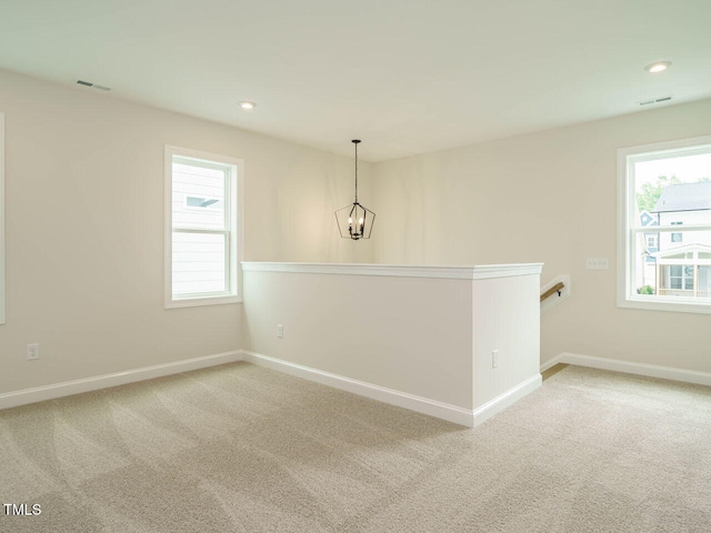 carpeted empty room with a wealth of natural light and a notable chandelier