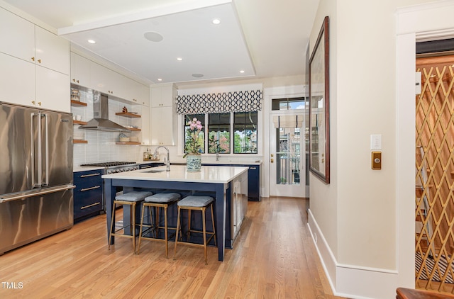 kitchen with wall chimney exhaust hood, a kitchen island with sink, high quality appliances, white cabinetry, and a breakfast bar area