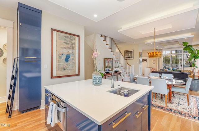 kitchen featuring sink, blue cabinets, an island with sink, pendant lighting, and light wood-type flooring