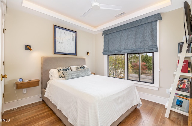 bedroom with hardwood / wood-style floors, ceiling fan, and a tray ceiling