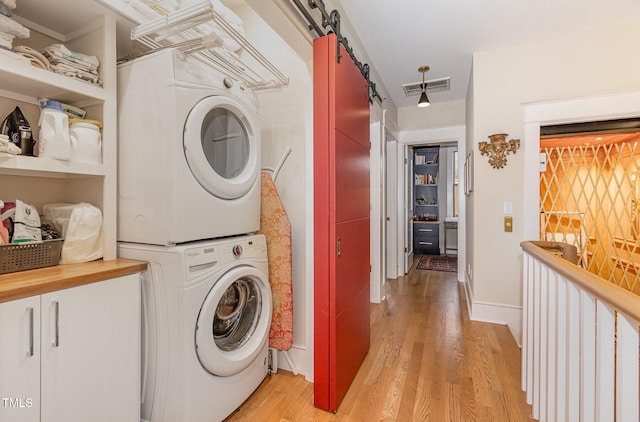 clothes washing area with a barn door, stacked washer and dryer, and light hardwood / wood-style flooring