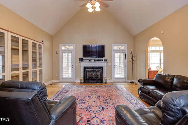 living room featuring ceiling fan, light hardwood / wood-style floors, high vaulted ceiling, and a fireplace