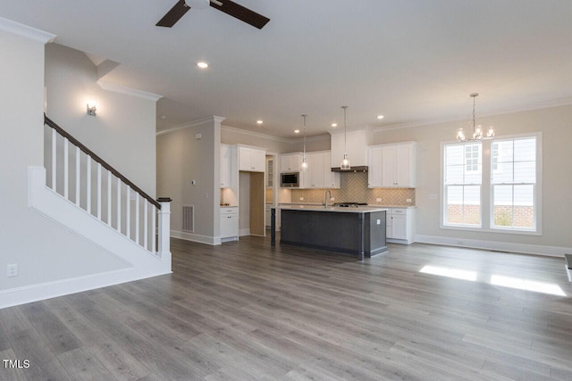 unfurnished living room featuring ceiling fan with notable chandelier, visible vents, stairway, and wood finished floors