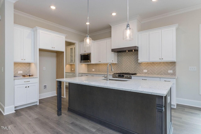 kitchen featuring crown molding, a center island with sink, stainless steel microwave, white cabinetry, and a sink