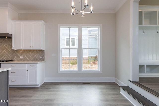 kitchen with wood finished floors, white cabinets, light countertops, ornamental molding, and tasteful backsplash