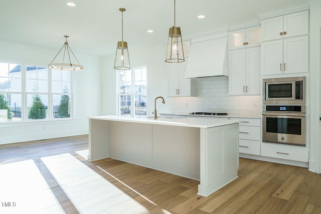 kitchen with a kitchen island with sink, white cabinets, light hardwood / wood-style floors, and appliances with stainless steel finishes