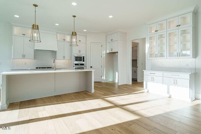 kitchen featuring white cabinets, light wood-type flooring, hanging light fixtures, and appliances with stainless steel finishes