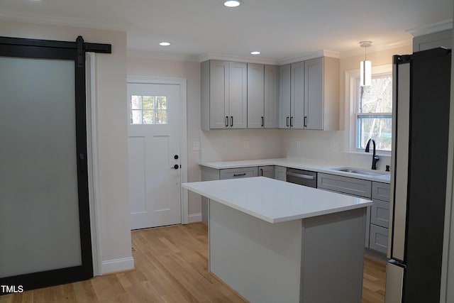 kitchen with a barn door, stainless steel appliances, a sink, ornamental molding, and gray cabinets