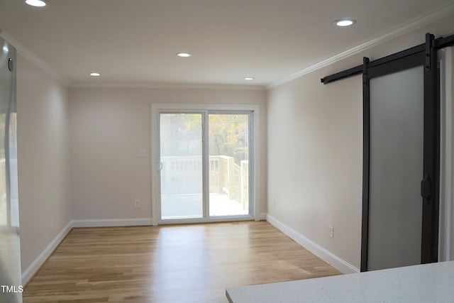 unfurnished room featuring baseboards, crown molding, light wood finished floors, and a barn door