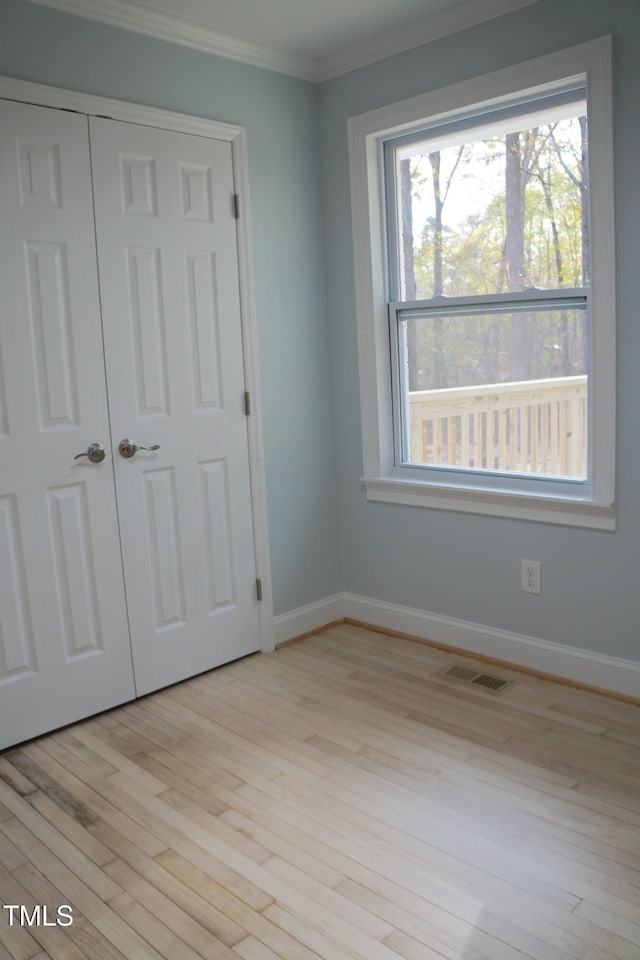 unfurnished bedroom with light wood-style flooring, visible vents, baseboards, ornamental molding, and a closet