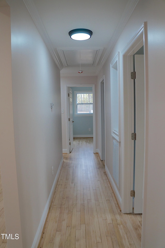 corridor featuring crown molding, baseboards, attic access, and light wood-style floors