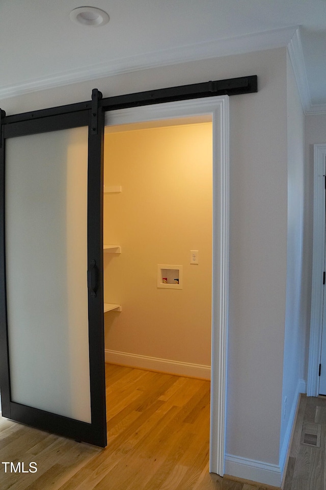 interior space featuring ornamental molding, a barn door, wood finished floors, and baseboards