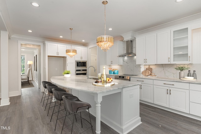 kitchen featuring a kitchen island with sink, pendant lighting, wall chimney range hood, and appliances with stainless steel finishes