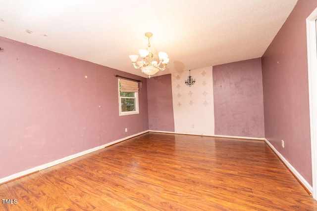 unfurnished room featuring wood-type flooring, a textured ceiling, and a chandelier