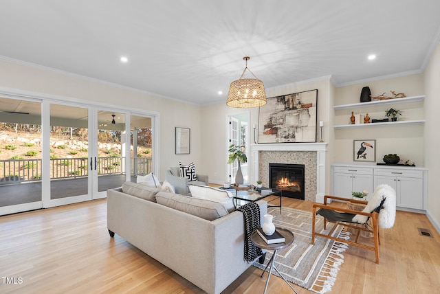 living room with a fireplace, light hardwood / wood-style floors, ornamental molding, and a notable chandelier