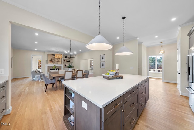 kitchen with ornamental molding, dark brown cabinets, decorative light fixtures, light hardwood / wood-style flooring, and a center island