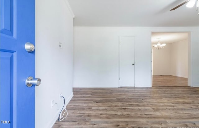 empty room with wood-type flooring, ceiling fan with notable chandelier, and ornamental molding