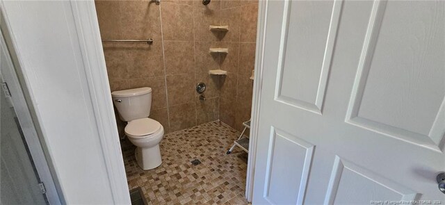 bathroom with a tile shower and toilet