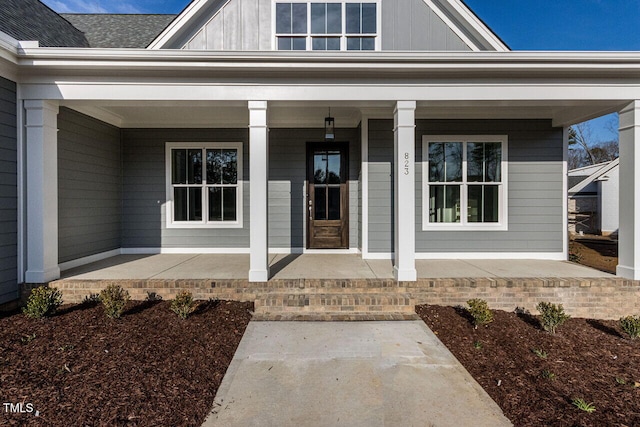 entrance to property featuring board and batten siding, covered porch, and roof with shingles