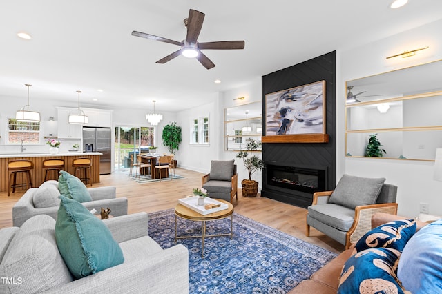 living room featuring ceiling fan with notable chandelier, a large fireplace, and light hardwood / wood-style flooring