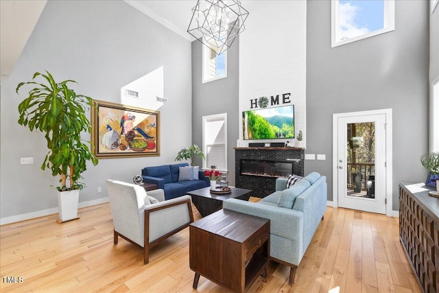 living room with light wood-type flooring, a towering ceiling, crown molding, and a healthy amount of sunlight