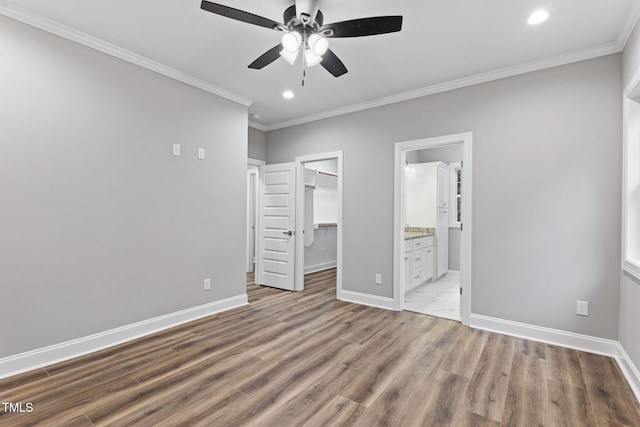 unfurnished bedroom featuring connected bathroom, a spacious closet, crown molding, a closet, and light wood-type flooring