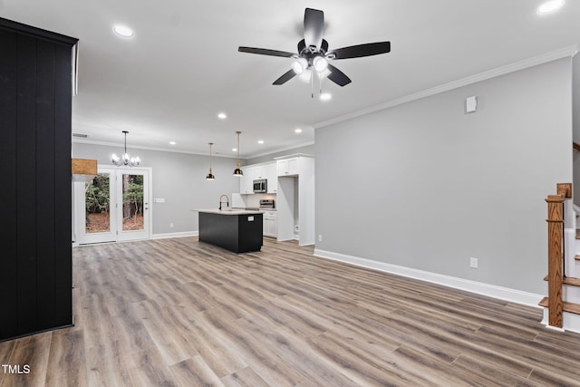 unfurnished living room featuring ceiling fan with notable chandelier, light wood-type flooring, and ornamental molding