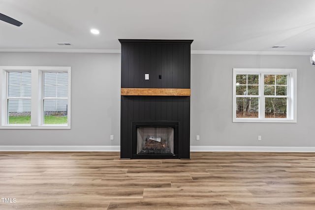 unfurnished living room featuring ceiling fan, a large fireplace, light hardwood / wood-style floors, and ornamental molding