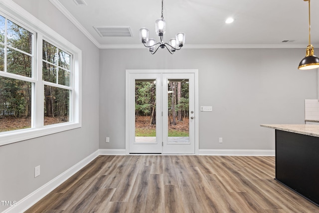 unfurnished dining area featuring a notable chandelier, wood-type flooring, ornamental molding, and a wealth of natural light