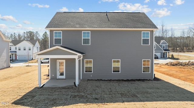 rear view of house with roof with shingles and a patio area