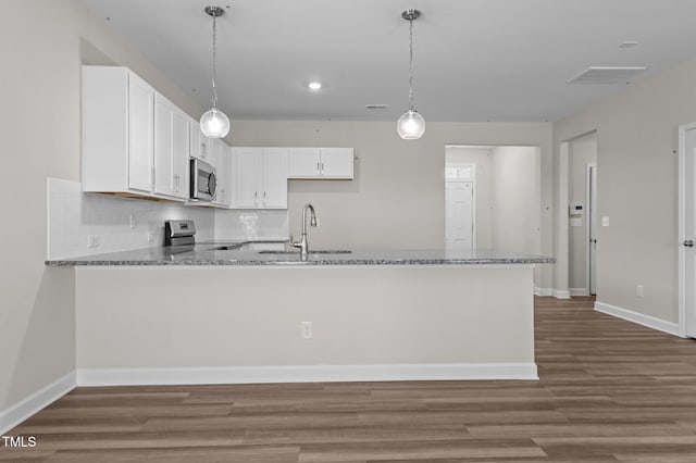 kitchen featuring decorative light fixtures, stainless steel appliances, white cabinets, a sink, and a peninsula