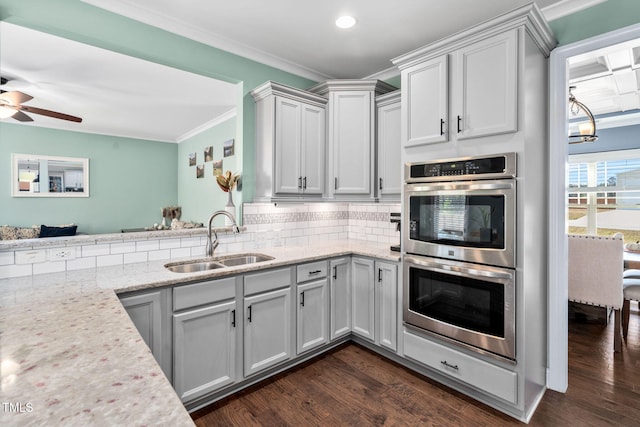 kitchen with light stone countertops, ornamental molding, stainless steel double oven, sink, and dark hardwood / wood-style floors