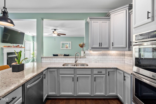 kitchen with appliances with stainless steel finishes, light stone counters, ceiling fan, sink, and pendant lighting