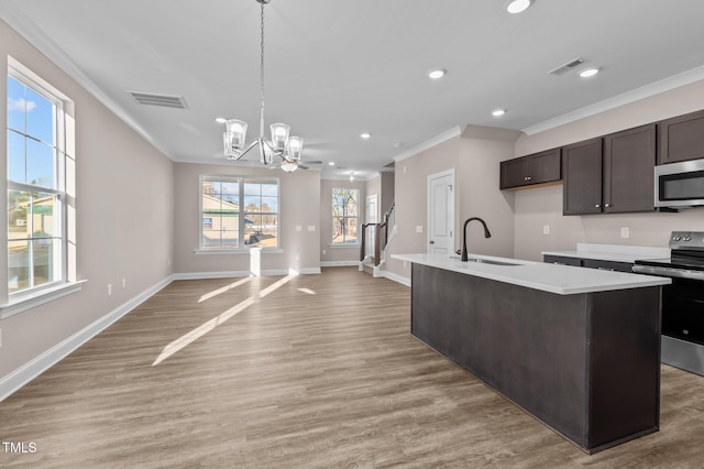 kitchen with a center island with sink, sink, ornamental molding, appliances with stainless steel finishes, and a notable chandelier