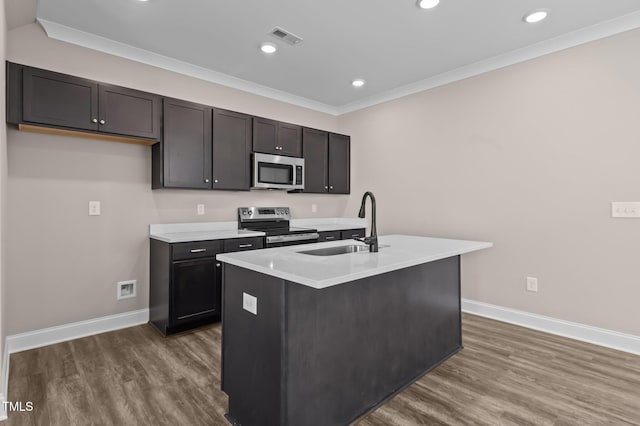 kitchen featuring appliances with stainless steel finishes, ornamental molding, a kitchen island with sink, sink, and hardwood / wood-style floors